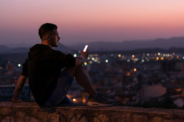 Man is looking his smartphone at night, lights of the city are on background