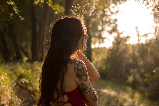 Portrait of a young girl in a red dress in a forest at sunset. Fantasy vibes