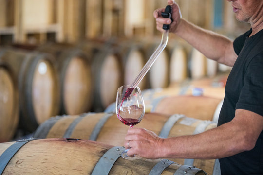 Cropped view of sommelier pouring wine from a barrel using a pipette - Powered by Adobe