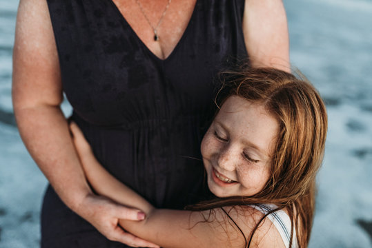 Side view of happy young daughter hugging mother in ocean at dusk