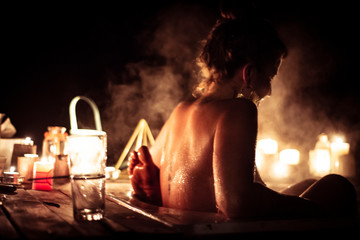 Young woman in steamy outdoor bath with partner by candle light