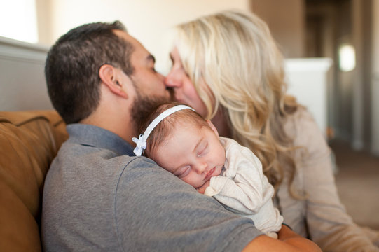 Close up of newborn baby sleeping with parents kissing in background