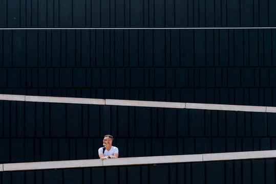Thoughtful bearded mature man in t-shirt leaning on stoned fence looking away against pattern wall