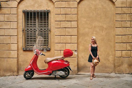 Stylish female standing by red scooter