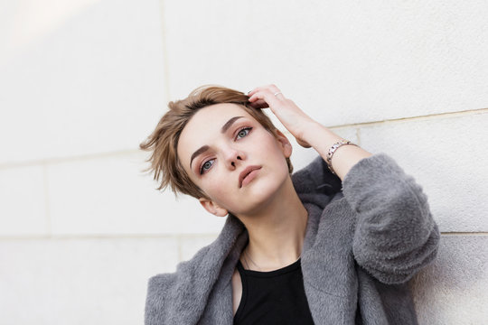 woman in gray coat adjusts her stylish short hairstyle