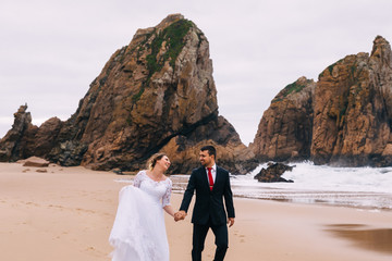 newlyweds hold hands and have fun on the sandy shore of the ocea