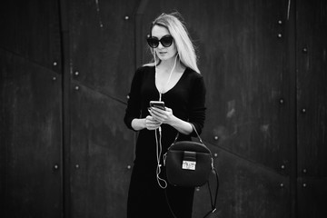 Image of beautiful business woman holding mobile phone. Young woman standing at the street and using mobile phone.Woman listening to music with the phone