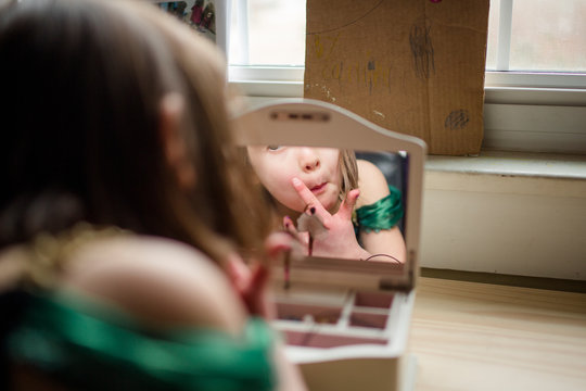 A little girl looks at her reflection in a jewelry box mirror