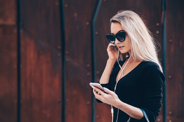 Image of beautiful business woman holding mobile phone. Young woman standing at the street and using mobile phone.Woman listening to music with the phone