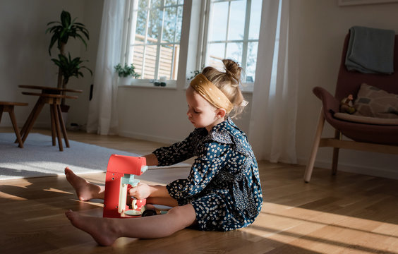 young girl playing with pretend coffee set at home in window light