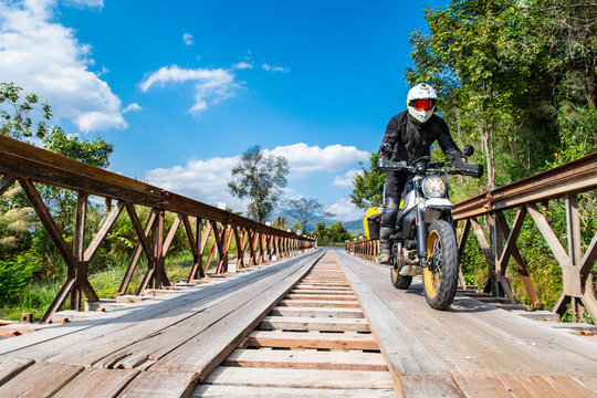 Man driving his scrambler type motorcycle over temporary bridge
