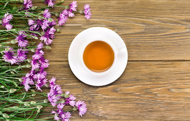 Fototapeta na wymiar Black tea in cup with pink cornflowers on a wooden background. Top view. Copy space.