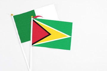 Guyana and Algeria stick flags on white background. High quality fabric, miniature national flag. Peaceful global concept.White floor for copy space.
