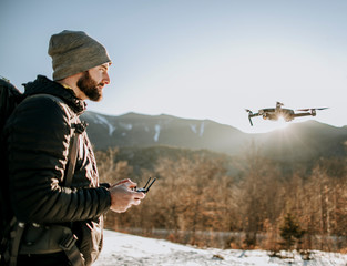 A man with a beard flies a drone in the mountains in winter.