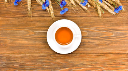 Tea in a cup with blue cornflowers and wheat ears on a wooden background. Copy space. Top view.