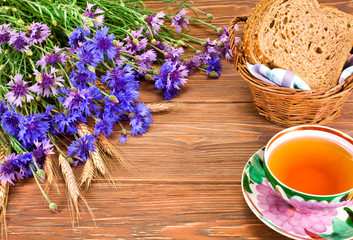 Tea cup with basket of bread, cornflowers and ears on a wooden background. Copy space.