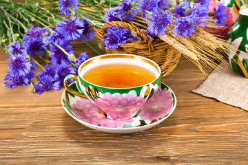 Teacup with the cornflowers and the wheat ears on a wooden background.