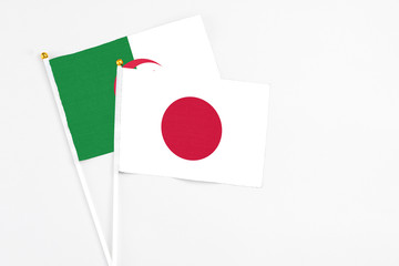 Japan and Algeria stick flags on white background. High quality fabric, miniature national flag. Peaceful global concept.White floor for copy space.