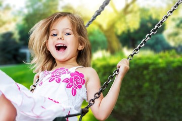Little child blond girl having fun on a swing