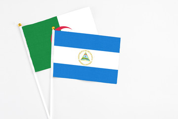 Nicaragua and Algeria stick flags on white background. High quality fabric, miniature national...