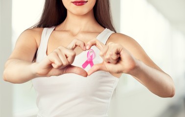 Heart framing from fingers on woman chest with pink badge to support breast cancer cause