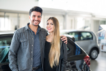 Fototapeta na wymiar Happy couple in front of their new car in a showroom