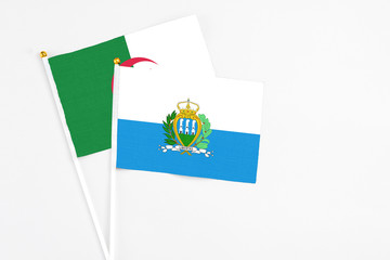 San Marino and Algeria stick flags on white background. High quality fabric, miniature national flag. Peaceful global concept.White floor for copy space.