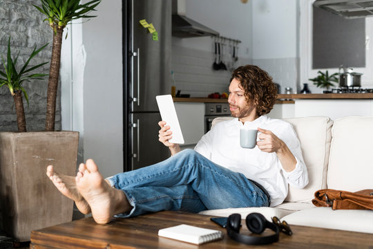 Relaxed man sitting on couch at home using tablet