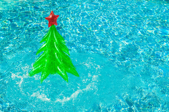 Inflatable Christmas tree splashing out of sparkling blue swimming pool in a bright tropical holiday travel background