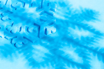 Winter background of thick 3-D snowflake on a bright blue background under the stylized shadow of another snowflake