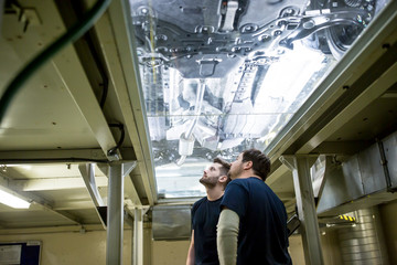 Two colleagues in factory checking underbody of a car - obrazy, fototapety, plakaty