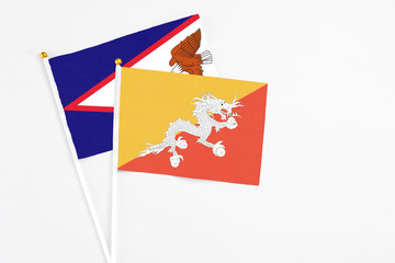 Bhutan and American Samoa stick flags on white background. High quality fabric, miniature national flag. Peaceful global concept.White floor for copy space.