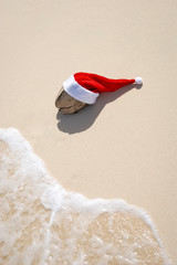 Weathered old coconut wearing a Santa hat taking a holiday break on sunny sand beach