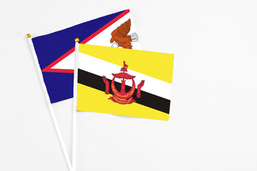 Brunei and American Samoa stick flags on white background. High quality fabric, miniature national flag. Peaceful global concept.White floor for copy space.