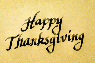 Fototapeta na wymiar Happy Thanksgiving message handwritten in black calligraphy script on textured gold paper