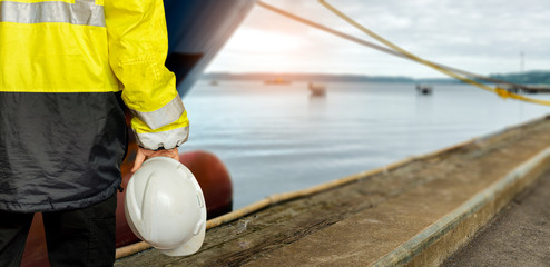 Ship supervisor engineer inspector stands at the dockside in a port. Wearing safety helmet and...