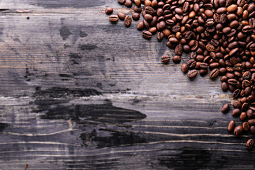 Roasted brown coffee beans scattered on wood textured table with a lot copy space for text. Flat lay composition. Close up, top view, background.