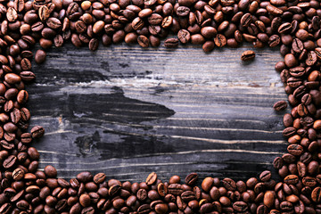 Roasted brown coffee beans scattered on wood textured table with a lot copy space for text. Flat lay composition. Close up, top view, background.