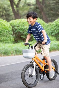 Happy little Chinese boy riding bike in park