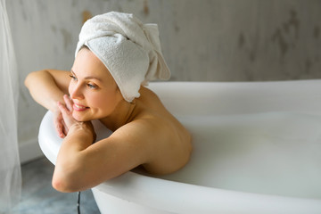 beautiful young woman with a towel on her head washes in a bath with milk