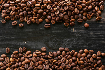 Roasted brown coffee beans scattered on wood textured table with a lot copy space for text. Flat lay composition. Close up, top view, background.