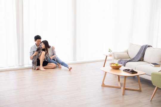 Happy young Chinese couple playing with dog in living room