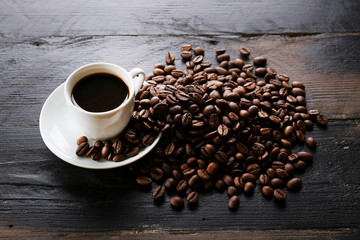 Coffee cup with roasted brown beans scattered on wood textured table with a lot copy space for text. Flat lay composition. Close up, top view, background.