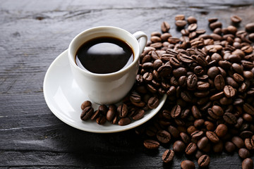 Coffee cup with roasted brown beans scattered on wood textured table with a lot copy space for text. Flat lay composition. Close up, top view, background.