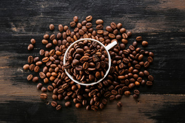 Coffee cup with roasted brown beans scattered on wood textured table with a lot copy space for text. Flat lay composition. Close up, top view, background.