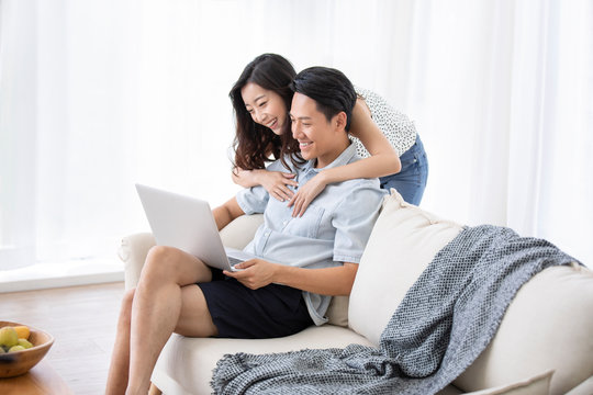 Happy young Chinese couple using laptop in living room