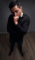 Sexy thinking brutal man looking serious in black shirt on grey studio background. Closeup