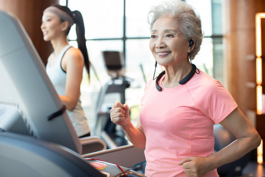 Senior Chinese woman running with wireless headphone at gym