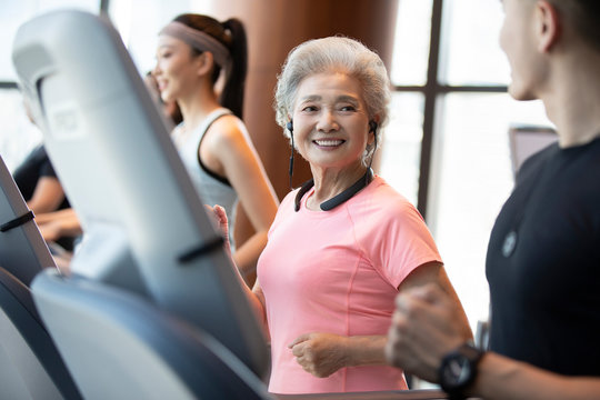 Senior Chinese woman running with wireless headphone at gym