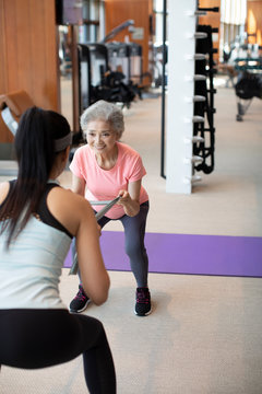 Senior Chinese woman working out with personal trainer at gym